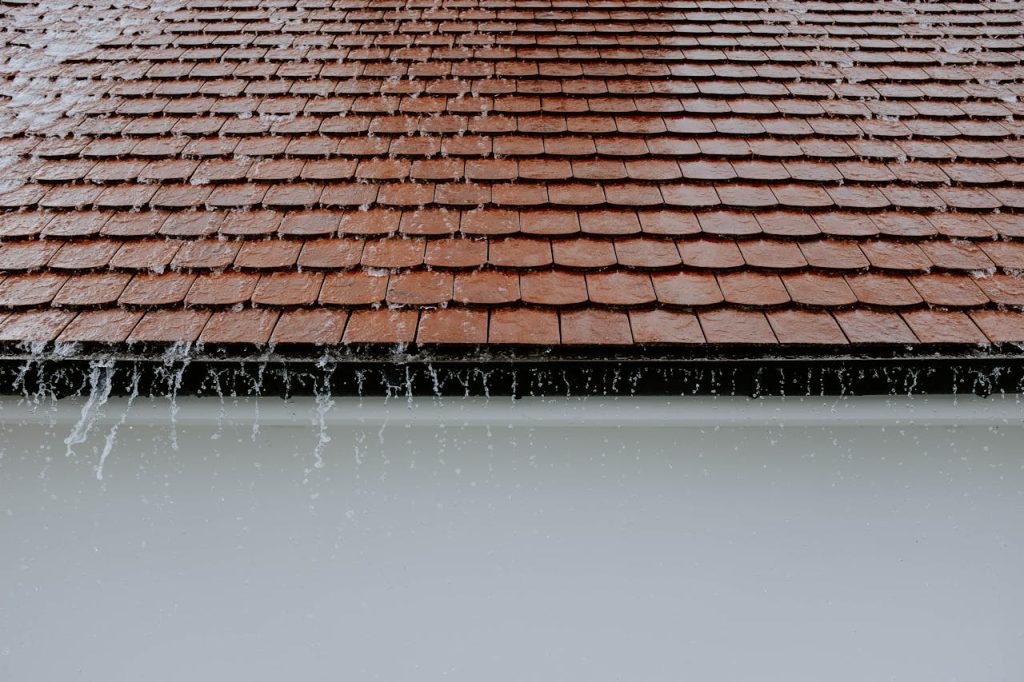 Dach läuft über Brown roof tiles with rainwater cascading down, showcasing architectural texture and detail.