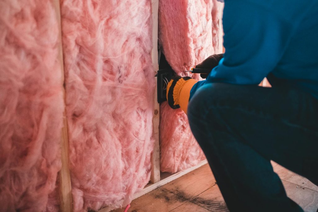 pexels photo 6124239 6124239 Focused worker installing pink fiberglass insulation in a building interior.